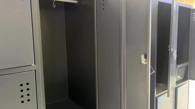 Open grey metal lockers in locker room, empty compartments with hanging bar for secure personal storage