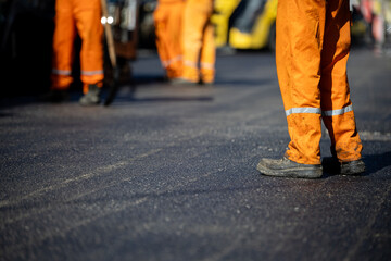 Construction workers in orange uniforms laying asphalt on a busy road during daylight hours
