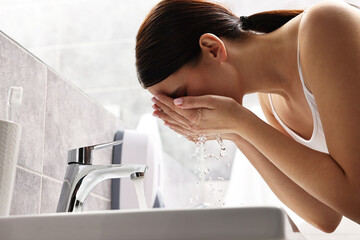 Woman washing her face over sink in bathroom, low angle view
