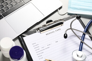 Medical card form, pills, laptop and stethoscope on grey table, above view