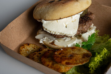 juicy burger with meat patty, cheese in kraft packaging on light background, close up view