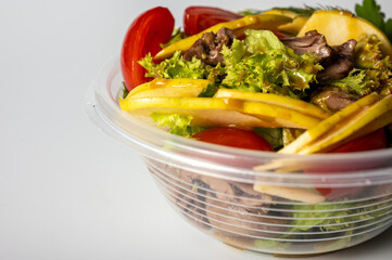 summer salad, tomato salad, vegetables, in a plastic container on a light background, food delivery, takeaway food