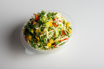 Fresh cabbage salad with bell pepper, corn, green onion, and dill in a plastic container. Healthy vegan food, vibrant and nutritious meal. Clean white background