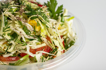 Fresh cabbage salad with bell pepper, corn, green onion, and dill in a plastic container. Healthy vegan food, vibrant and nutritious meal. Clean white background