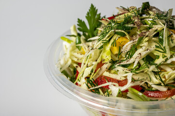 Fresh cabbage salad with bell pepper, corn, green onion, and dill in a plastic container. Healthy vegan food, vibrant and nutritious meal. Clean white background