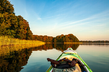 Kayak gliding across a tranquil lake, trees and reeds bathed in the golden light of the setting sun. 
