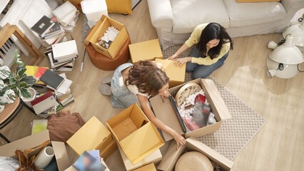 Happy couple sitting at living room with cardboard box while picking furniture from box. Top view of lesbian lover talking together while moving to new apartment or new estate. Girl love. Myrmidon.