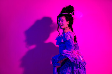 Elegant woman in historical costume standing in neon pink lighting with a sense of elegance and allure