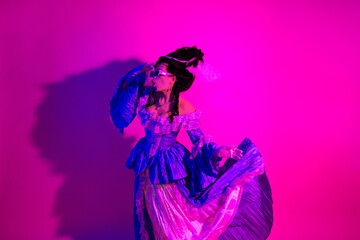 Fototapeta premium Elegant woman in baroque-inspired outfit against vibrant pink neon backdrop highlighting historic and modern blend