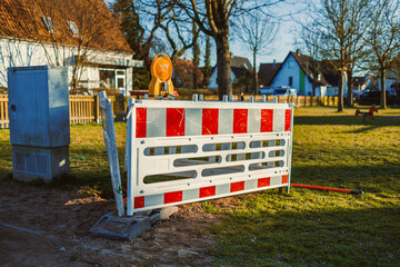 In a busy residential area, a construction barrier with a blinking warning light signals ongoing...
