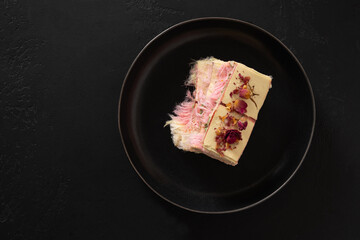 Trendy delicate white, pink chocolate with layer of white and pink pismaniye in plate on black background. Tasty dessert. View from above. Copy space.