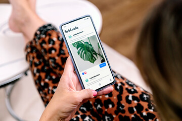Social Media ads on mobile phone screen. Woman with smartphone showing advertising example in a...