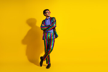 Stylish young man in a colorful suit poses confidently against a vibrant yellow background,...
