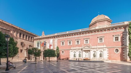 Panorama showing Patriarch's College Square in Valencia timelapse, featuring the historic Museo del Patriarca, fountain with sculptures and Church of the Patriarch. Clear blue sky, Spain.