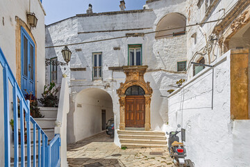 Scenic view of Ostuni, Italy's 'White City,' showcasing whitewashed buildings under a clear blue sky, with narrow streets and historic architecture illuminated by sunlight.