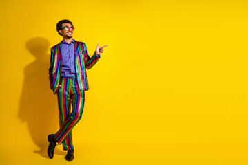 Charismatic young man in a rainbow-striped suit posing against a bright yellow background, exuding...
