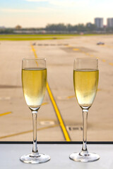 Two flute glasses of champagne in front of a window of an airport business class lounge. No people.