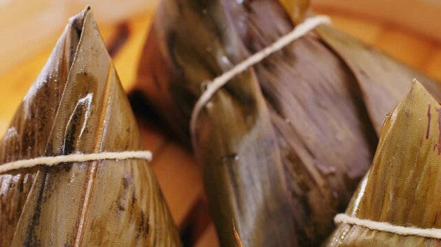 Hand holding zongzi (rice dumpling) with savoury fillings wrapped in bamboo or reed leaves.