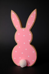 Pink wooden Easter bunny decoration with white polka dots and a fluffy tail against a dark background. 