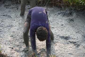 Obraz premium Young boys are catching fish by the hand in the muddy canal 
