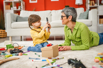 Grandchild take a photo of grandmother while she play wit toys at home
