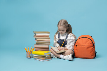 Schoolgirl with backpack and books on light blue background