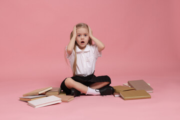 Emotional schoolgirl with books on pink background