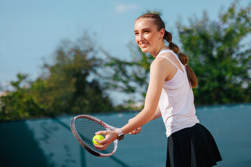 Happy teen tennis player preparing to serve on court in sunlight, smiling during practice.