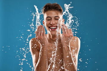 Smiling man washing his face on blue background