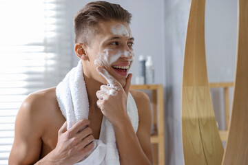 Man washing his face with cosmetic product near mirror in bathroom