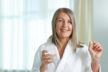 Smiling woman with collagen pill and glass of water at home. Space for text