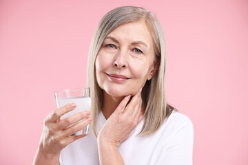 Woman with glass of collagen water on pink background