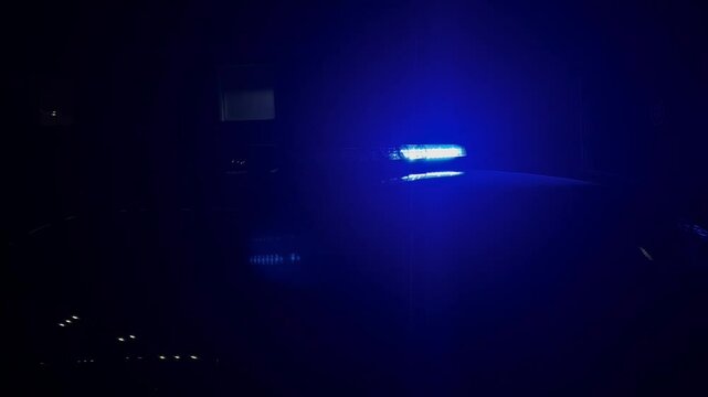 Blue emergency light bar glowing on a police car roof at dark night. Flashing blue LED siren light bar of emergency vehicle in the darkness concept of security, crime scene and law enforcement. 