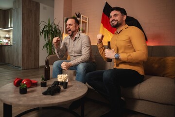 Obraz premium Friends celebrating victory while watching sports match at home with snacks and drinks in cozy living room