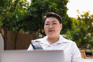 Young plus size Asian woman working outdoors on a laptop at a cafe during the day