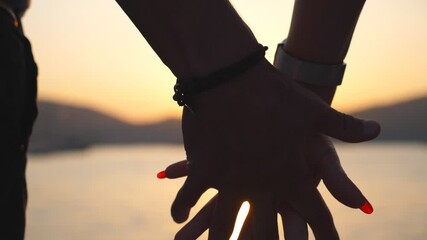 Male and female hands comforting and stroking each other at sunset against an sea background. Young couple joining arms outdoor. Summer vacation. Concept of loving and happiness. Close up Slow motion