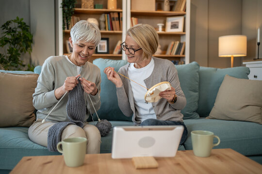 Senior women knitting and embroidering together at home with video tutorial