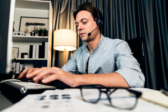 Call center consulting with customers on headphones on monitor in business paragraph with typing on pc with dynamic data marketing analysis planning at modern home office at night time. Pecuniary.