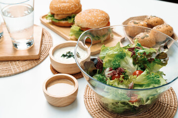 Fresh mix vegetable salad in glass blow beside dish of double meat hamburger and wholegrain bun on meal cooked by homemade serving white table. Preparing special dish menu list's restaurant. Infobahn.