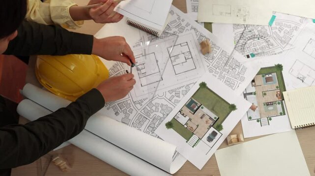 Architect and safety engineer discussion about building construction use blueprint on table with architectural document, measurement tool and wooden block scatter around at modern office. Delineation.