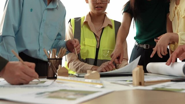 Smart architect and safety engineer discussion about building blueprint on table with architectural document, measurement tools and wooden block scatter around at modern office. Closeup. Delineation.