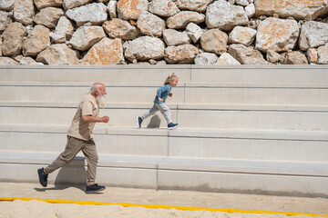 Energetic grandfather and young boy running up stone bleachers outdoors, showcasing...