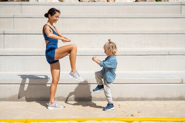 Fit mother and young son playfully exercising together outdoors, raising knees in sync while...