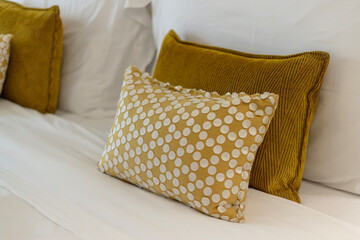 Brightly colored pillows sit on a neatly made bed, featuring a textured yellow pillow behind a decorative polka-dot pillow. The overall arrangement adds warmth to the room