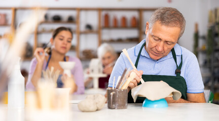 Mature man learns to carve figured dishes from clay