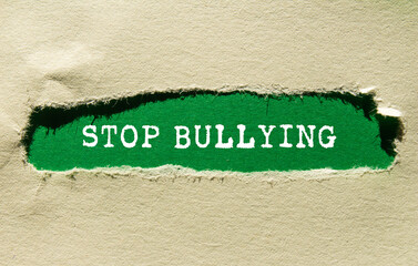 Stop bullying message written on ripped torn paper on green background. Conceptual stop bullying...