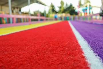 Colorful rubber running track with red, purple, yellow stripes and white line. Shot from a low...