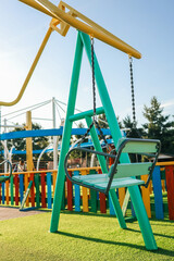 Empty swing seats at a vibrant colorful playground on a sunny day, with rainbow fence and play structures in the background