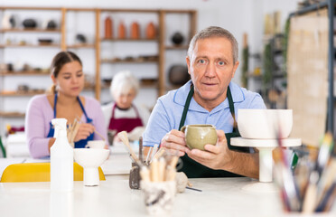 Satisfied mature man demonstrates pottery made by her own hands