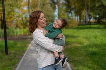 Fototapeta premium Caucasian woman holds her one-year-old son in her arms while walking in the park in autumn. 